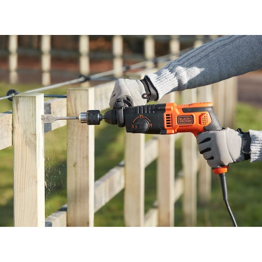 BLACKDECKER BEHS01 corded hammer drill in use, drilling wood outdoors with gloved hands.
