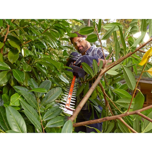 BLACKDECKER BEHTS401 hedge trimmer cutting green branches outdoors, close-up of blade in use.