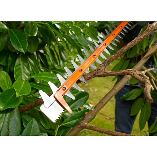 BLACKDECKER BEHTS501 hedge trimmer blade cutting a thick branch among green leaves outdoors.