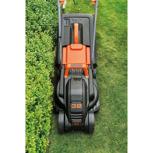 BLACKDECKER BEMW351GL2 lawn mower, black and orange, top view cutting grass near hedge.