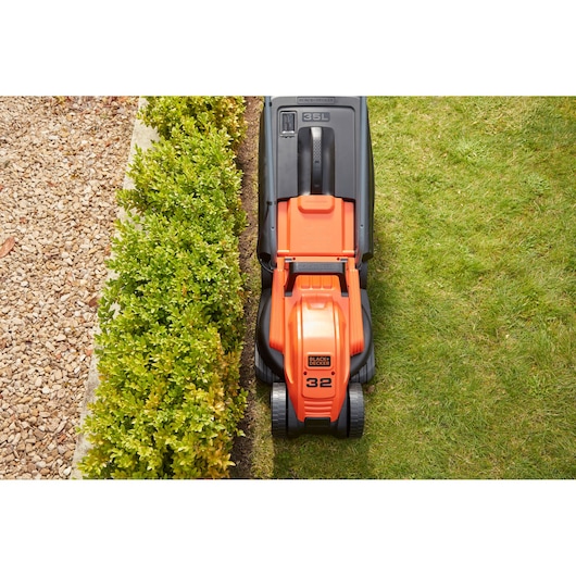 BLACK+DECKER BEMW451BH lawn mower top view cutting grass next to hedge and gravel path.