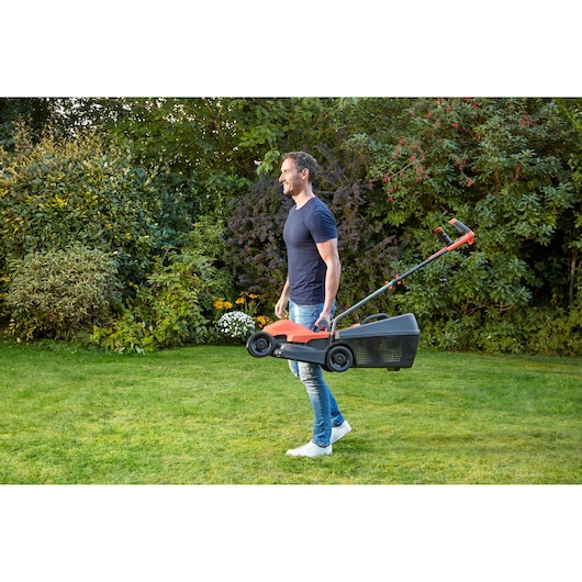 BLACK+DECKER BEMW451BH lawn mower being carried by a person in a garden, orange and black color.
