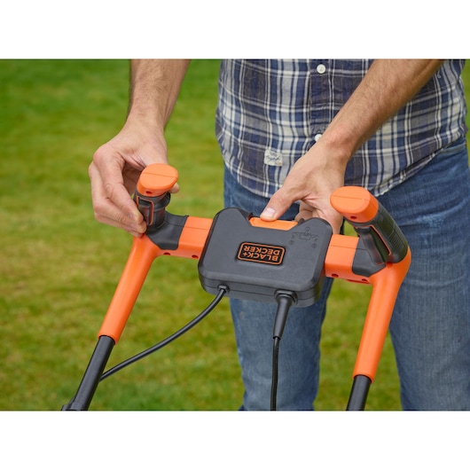 BLACK+DECKER BEMW451BH lawn mower handle with orange controls, close-up photo held by a person outdoors.