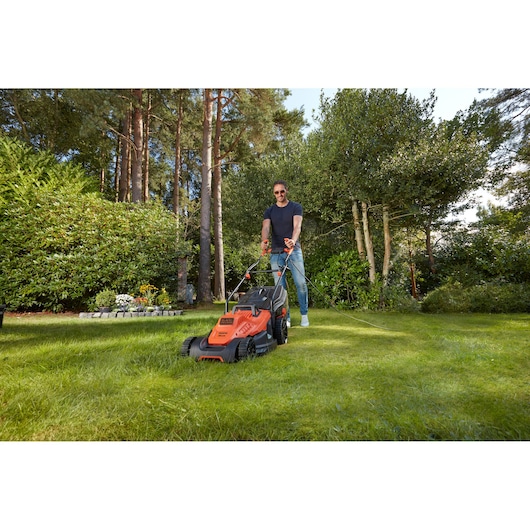 BLACKDECKER BEMW471BH lawn mower in use on a grassy yard, orange and black, front angle view.