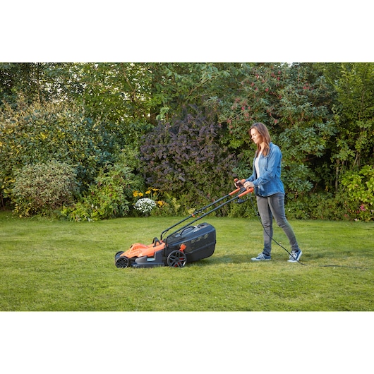 BLACKDECKER BEMW471BH lawn mower being used on grass in a garden, photographed from the side.