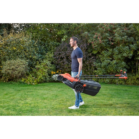 BLACKDECKER BEMW471BH lawn mower being carried by a person in a garden