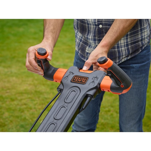 Close-up photo of BLACKDECKER BEMW471ES lawn mower handle and controls held outdoors by a person.