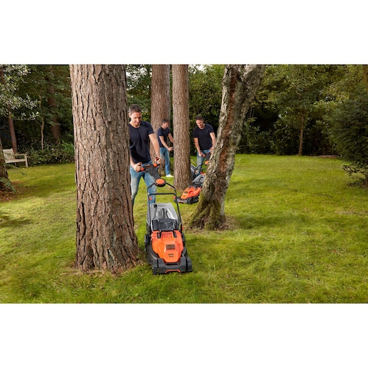 Photo of BLACKDECKER BEMW471ES lawn mower used on grass around trees in a garden setting.