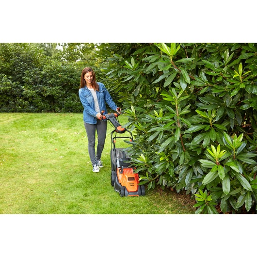 BLACKDECKER BEMW471ES lawn mower in use on grass near bushes outdoors.