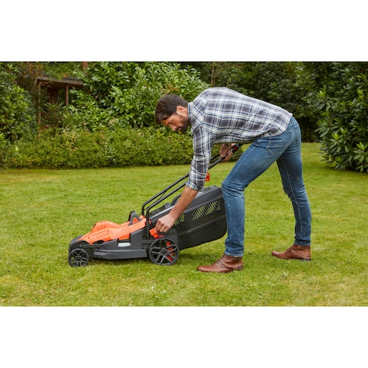 Photo of BLACKDECKER BEMW471ES lawn mower being adjusted on grass by a person outdoors.