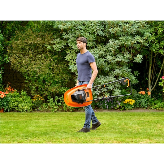Man carrying BLACKDECKER BEMWH551 orange hover lawn mower in garden.