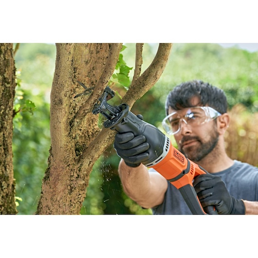 BLACKDECKER BES301 reciprocating saw cutting tree branch outdoors, person wearing gloves and safety glasses.