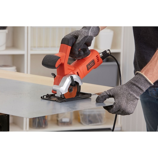 Photo of BLACKDECKER BES510K compact circular saw cutting metal sheet in workshop, operator wearing gloves.