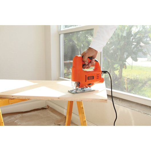 Photo of BLACKDECKER BES601 jigsaw cutting plywood near a window, held by a person in a white sleeve.