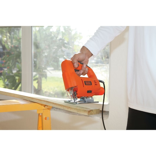 BLACKDECKER BES601 jigsaw cutting wood, handheld, orange body, indoor setting, product in use.