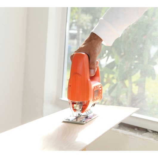 Photo of a BLACK+DECKER BES601 jigsaw cutting light wood, handheld indoors near a window.