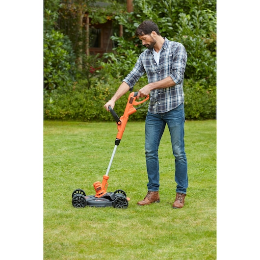 BLACKDECKER BESTA530CM orange grass trimmer with wheeled base being used outdoors on a lawn.