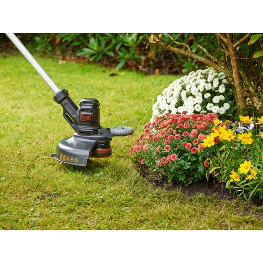BLACKDECKER grass trimmer BESTE628 next to flower bed on lawn, garden photography.