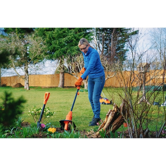 BLACKDECKER BETL1820L garden tiller used outdoors by person wearing orange gloves.