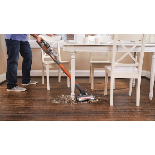 BLACKDECKER BHFEV182B cordless stick vacuum cleaning debris from hardwood floor under dining table.