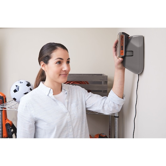 Photo of BLACKDECKER BHFEV182B battery charging on wall-mounted charger in a home setting.