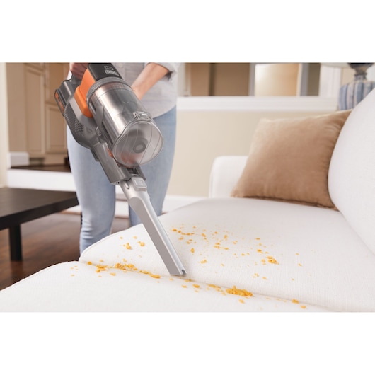 BLACKDECKER BHFEV182C cordless vacuum cleaning crumbs from a white sofa in a home setting.