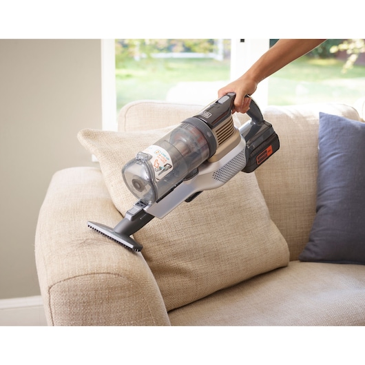 BLACKDECKER BHFEV36B2D cordless vacuum cleaner used on a beige sofa in a living room.