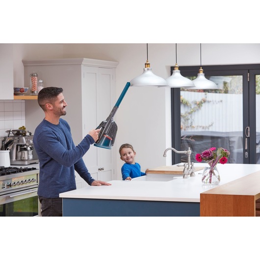 BLACK+DECKER BHHV320B cordless handheld vacuum used to clean a hanging lamp in a modern kitchen.