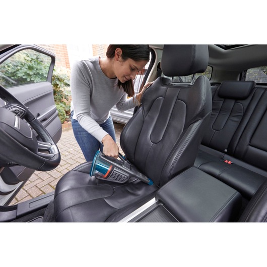 BLACKDECKER BHHV320B handheld vacuum cleaning black leather car seat, indoor usage photography.