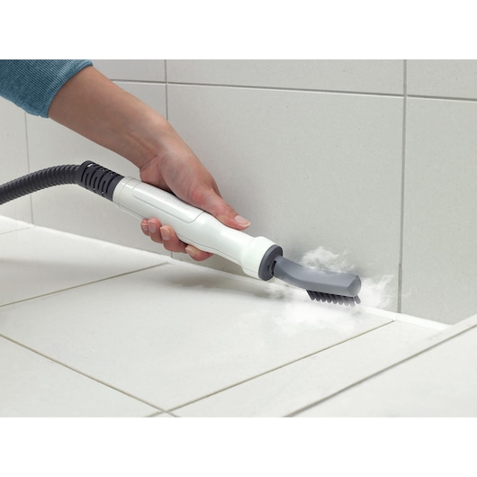 BLACKDECKER BHSM1610DSM steam cleaner handheld attachment with brush cleaning grout between white tiles.
