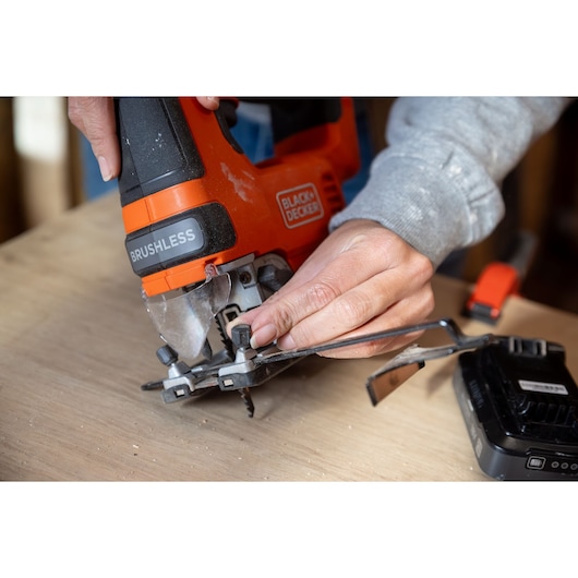 Close-up of BLACKDECKER BLCJS78N cordless jigsaw being adjusted by hand on wood surface.