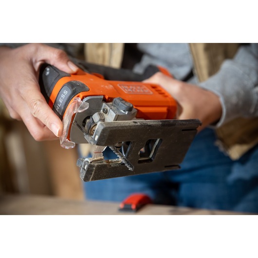 Close-up photo of BLACKDECKER BLCJS78N cordless jigsaw in use, orange and black body, visible saw blade.