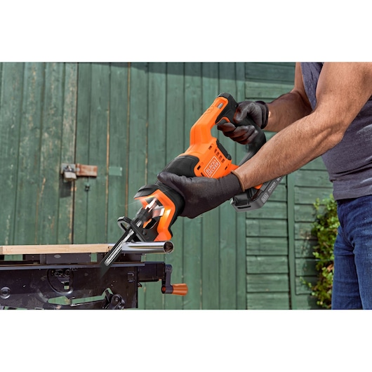Photo of BLACK+DECKER BLCR78N reciprocating saw in use cutting metal, orange and black design, outdoor setting.