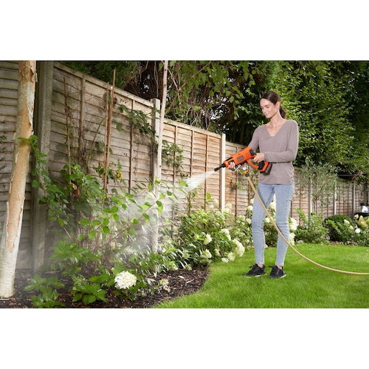 Photo of BLACK+DECKER BZOSW1 portable power washer spraying water on garden plants outdoors.