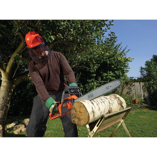 BLACKDECKER CS2245 chainsaw cutting log outdoors, person wearing safety gear.