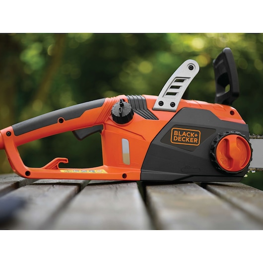 Photo of BLACK+DECKER CS2245 electric chainsaw, orange and black, side view on wooden table outdoors.