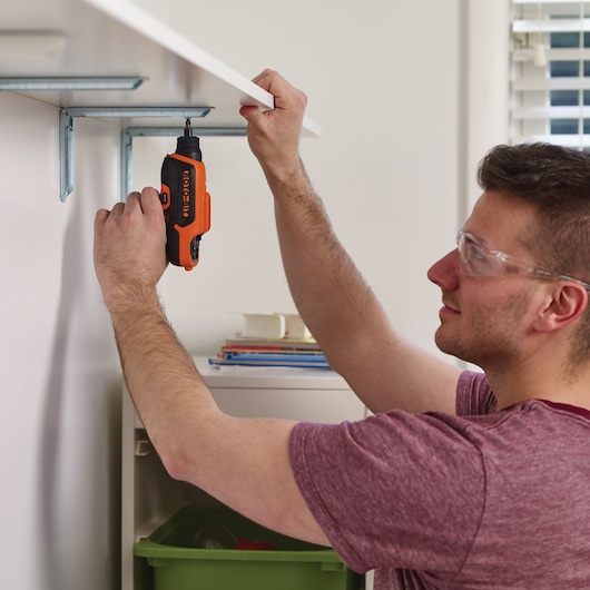 BLACKDECKER CS36BSC orange cordless screwdriver used to install a shelf bracket indoors.