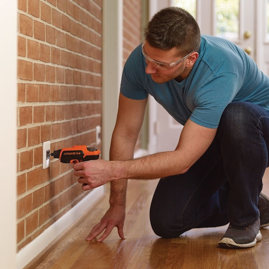 BLACKDECKER CS36BSC cordless screwdriver used on wall outlet, orange and black, home setting.