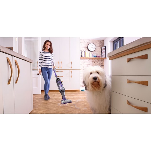 BLACKDECKER CUA525BHP upright vacuum in use cleaning parquet floor near a white dog in a modern kitchen.