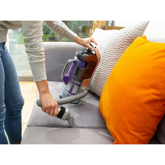 Photo of BLACKDECKER CUA525BHP vacuum cleaner with hose attachment cleaning a grey sofa with bright orange cushion.