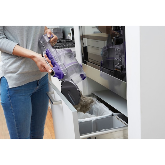 BLACKDECKER CUA525BHP vacuum canister being emptied into kitchen trash bin, product held by person.
