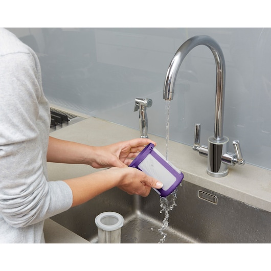 BLACKDECKER CUA525BHP vacuum filter being rinsed at kitchen sink, purple frame, product category photography