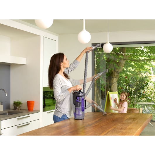 BLACKDECKER CUA525BHP upright vacuum cleaner cleaning a kitchen pendant light and wooden table.