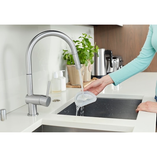 Photo of a person rinsing the BLACK+DECKER DVA325JP07 with water in a modern kitchen sink, side angle.