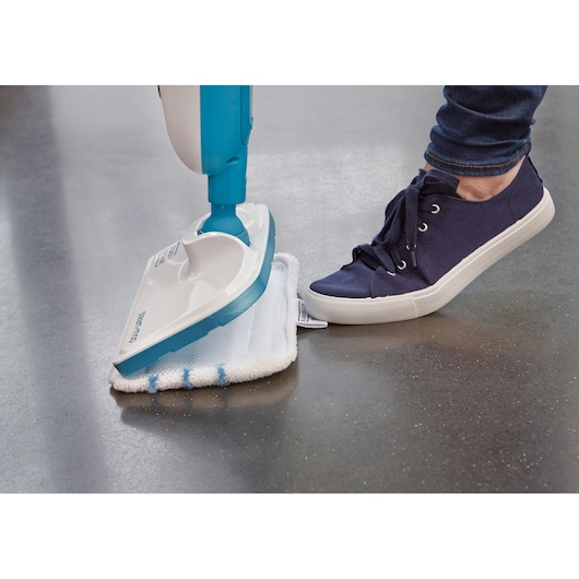 BLACKDECKER FSM13E1 steam mop with white and blue cleaning pad, close-up on grey floor, foot pressing pad.