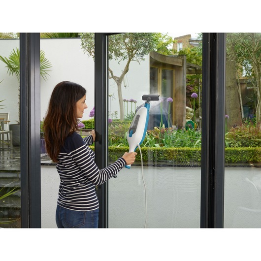 BLACKDECKER FSMH13E5 steam cleaner used on large glass doors in a garden setting.