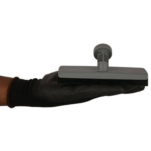 A person wearing a black glove is holding a rectangular grey cleaning attachment with a handle, viewed from the side against a white background.