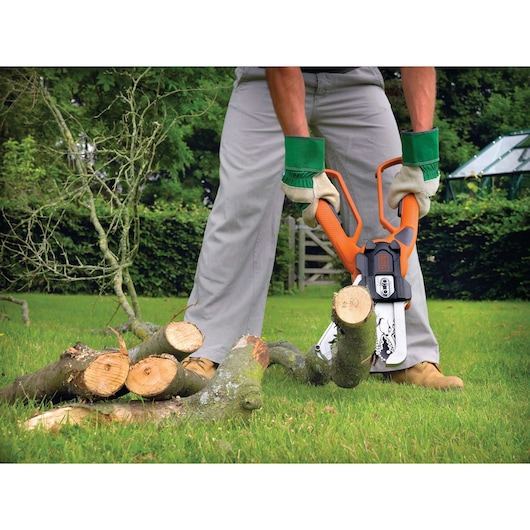 BLACK+DECKER GK1000 electric lopper cutting tree branches outdoors, shown in use with orange handles and gloves.