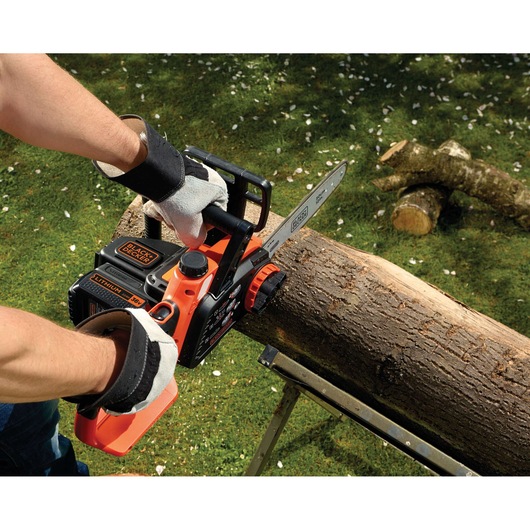 BLACK+DECKER GKC3630L20 chainsaw cutting a large tree branch outdoors, close-up of hands and tool in use.