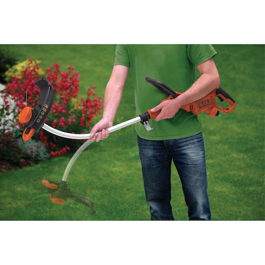 Photo of BLACK+DECKER GL7033 grass trimmer being held outdoors, orange and black design, curved shaft visible.